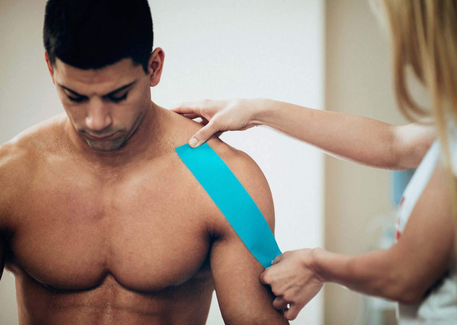 Physical therapist placing kinesio tape, placing it onto patient's shoulder